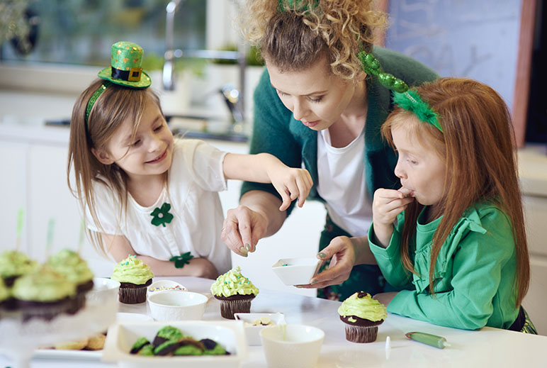Mom with two daughters making St. Patrick's Day cupcakes while they are wearing green accessories